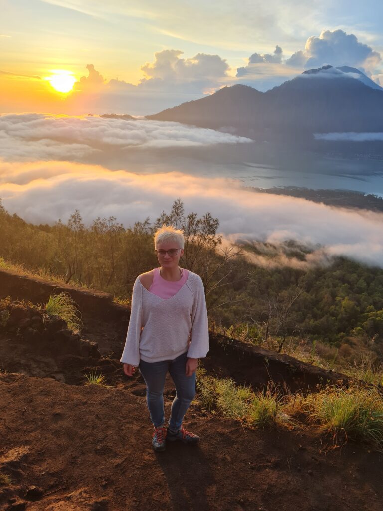 during your one week itinerary for Bali you must visit Mount Batur. Here seen: Standing atop the mountain with a beautiful backdrop of mountains and clouds covered in the red and yellow morning sun. 
