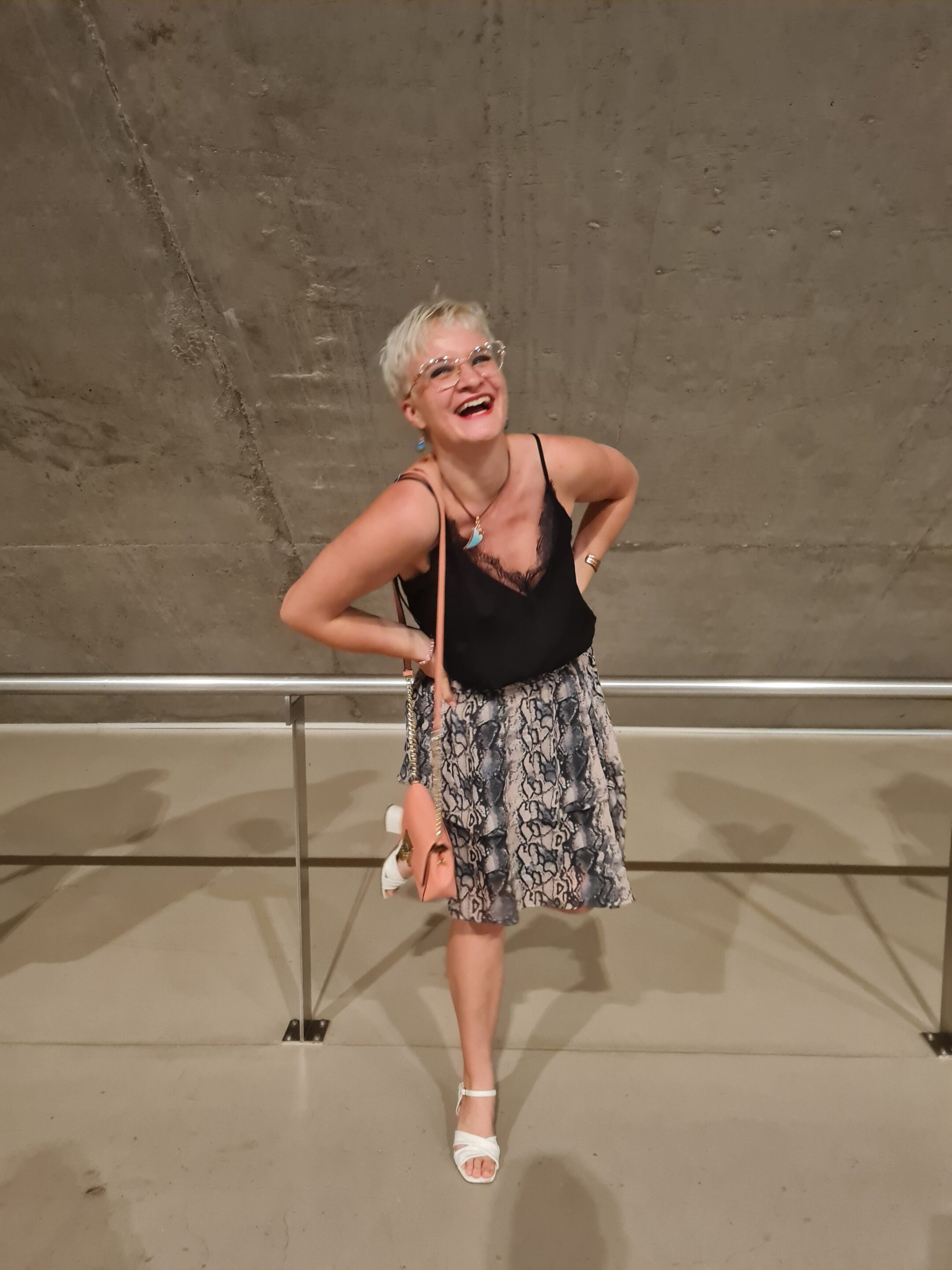 Woman laughing with a blue skirt, black shirt, and white shoes on. This pictures features an article on digital nomad money management.