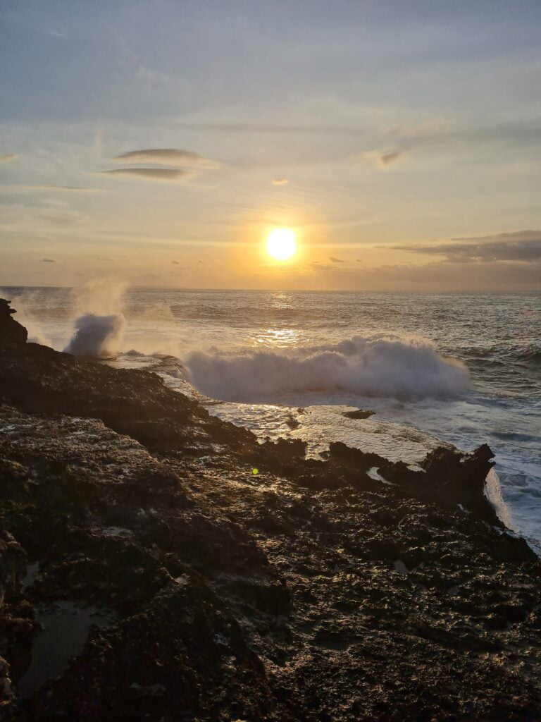 Sunsetting over the ocean. Waves crash into the volcanic rubble and coast line. 