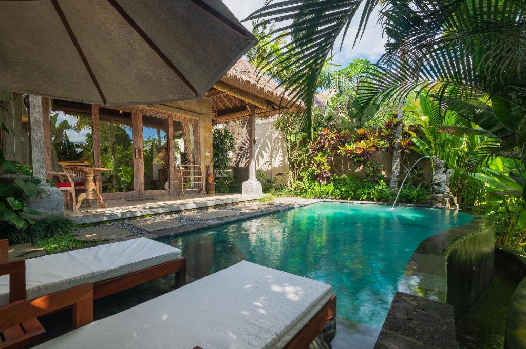 This is a display of a hotel in Ubud with private pool, Udaya Resorts and Spa. One can see two white pool beds in front, overlooking the pool which is an infinity pool. There is a beige umbrella on the top left corner of the image. One can also see a small villa in the background, towards the left. There is a terrace leading from the villa towards the private pool.